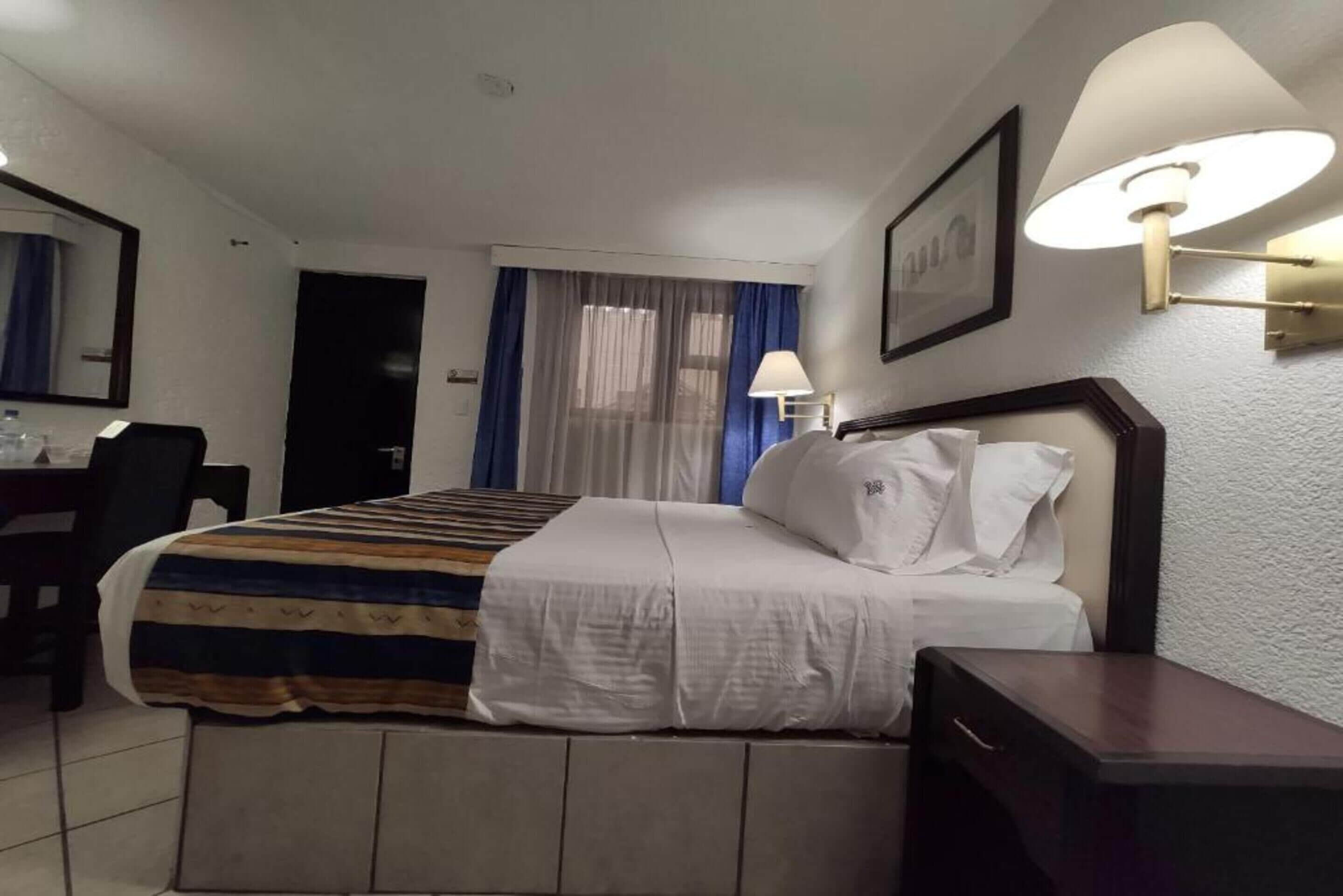 Una habitación de hotel con una cama, un escritorio, una silla y una lámpara.