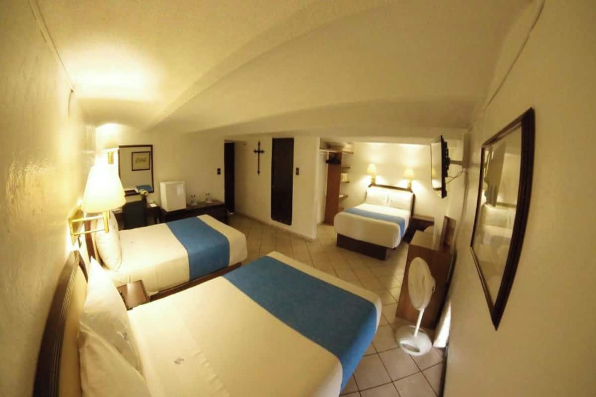 A hotel room with two beds, a desk, a chair, a mirror, and a cross on the wall.