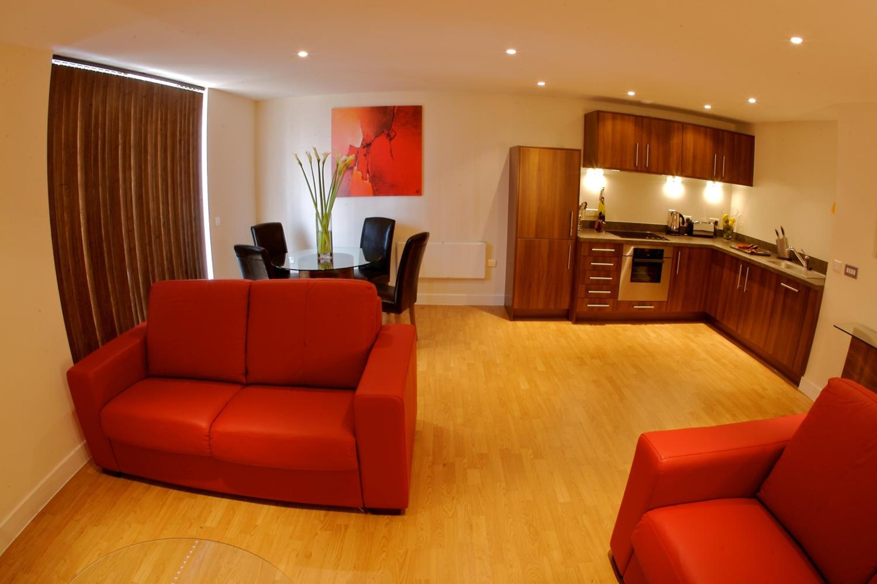 A modern living room with a red sofa, a dining table with chairs, and a kitchen area with wooden cabinets and a countertop.