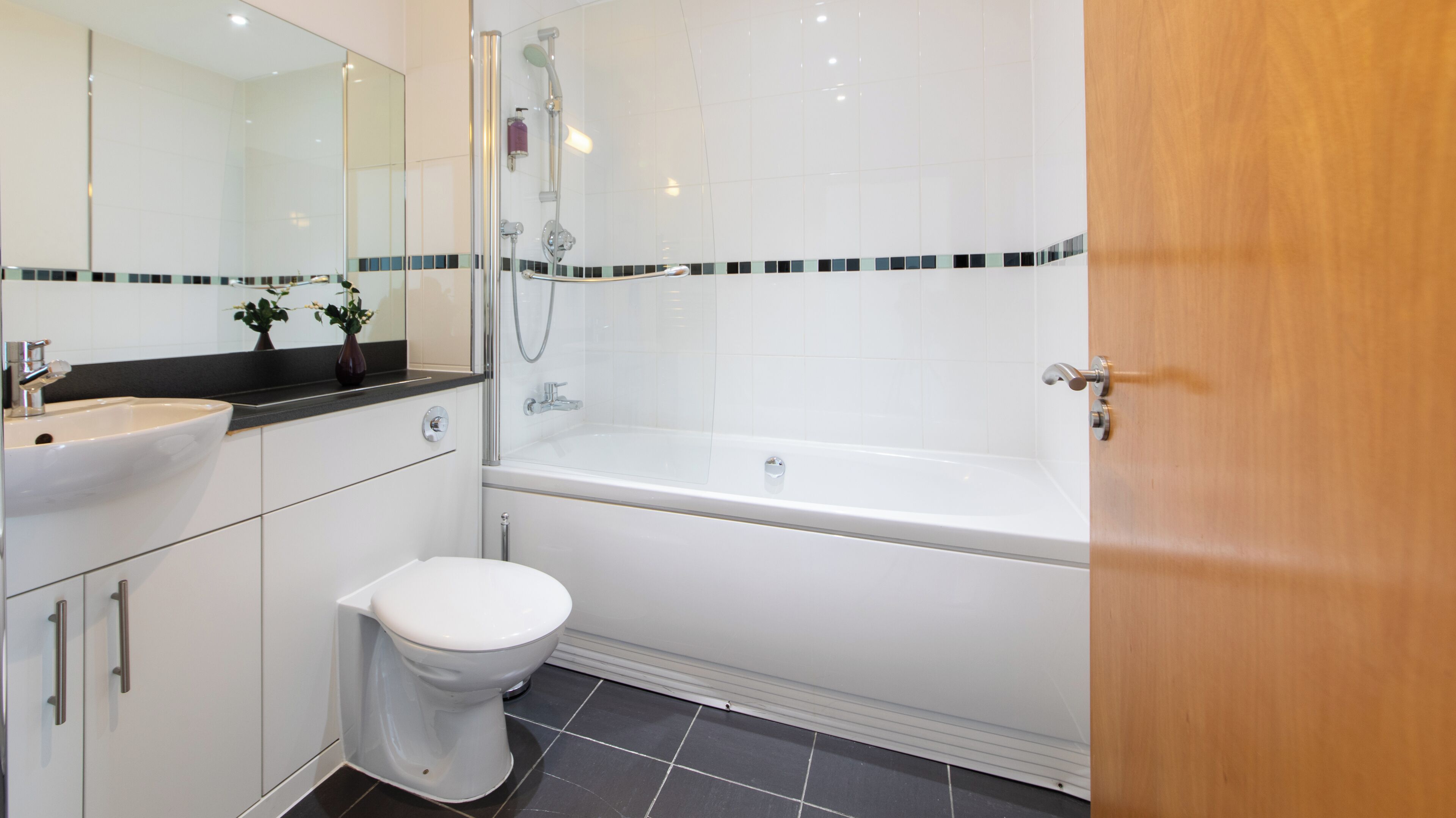 A modern bathroom with a white bathtub, a white toilet, and a sink with a mirror above it.