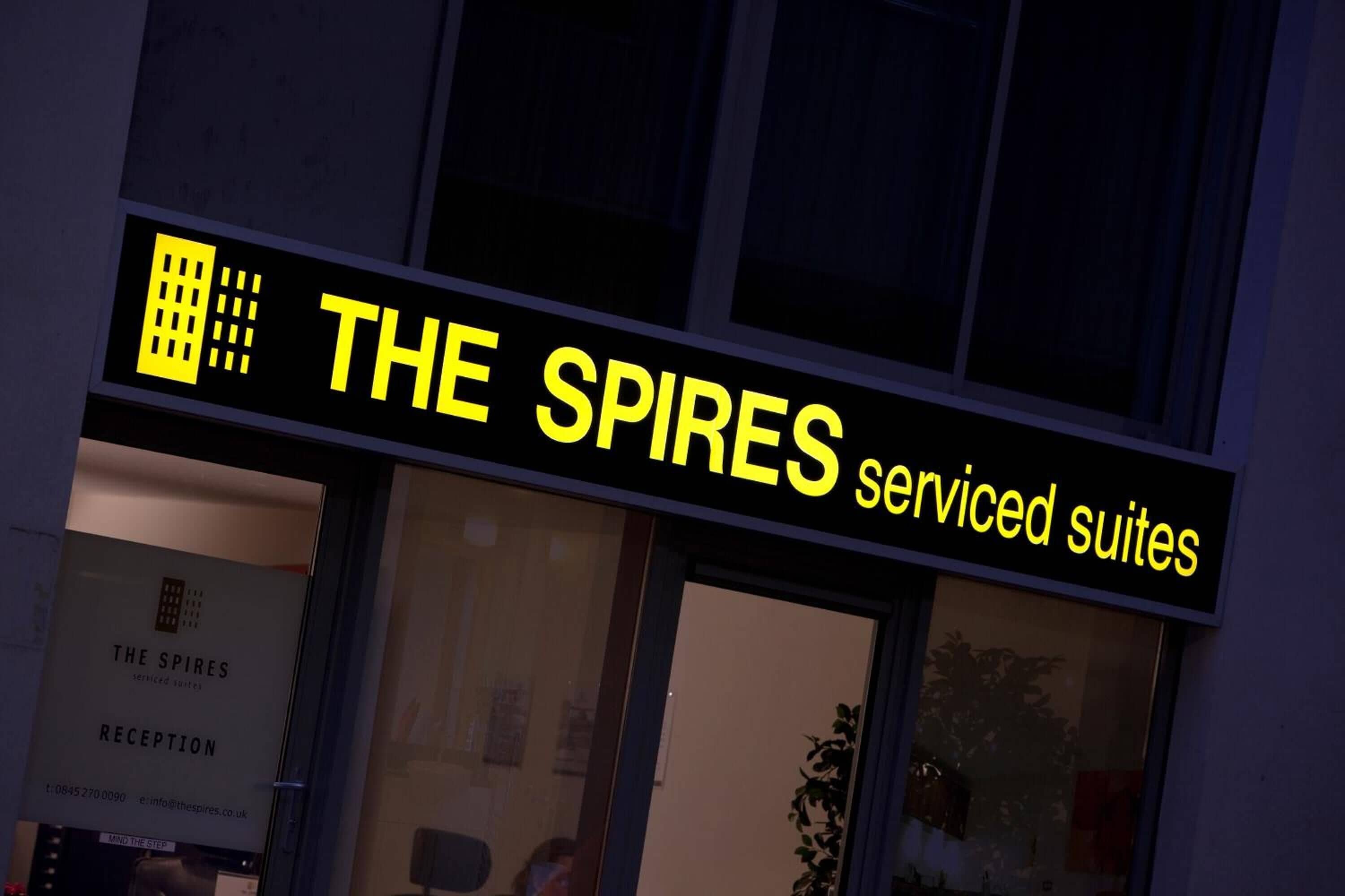 Une enseigne d’hôtel avec l’inscription « THE SPIRES serviced suites » en jaune sur fond noir.