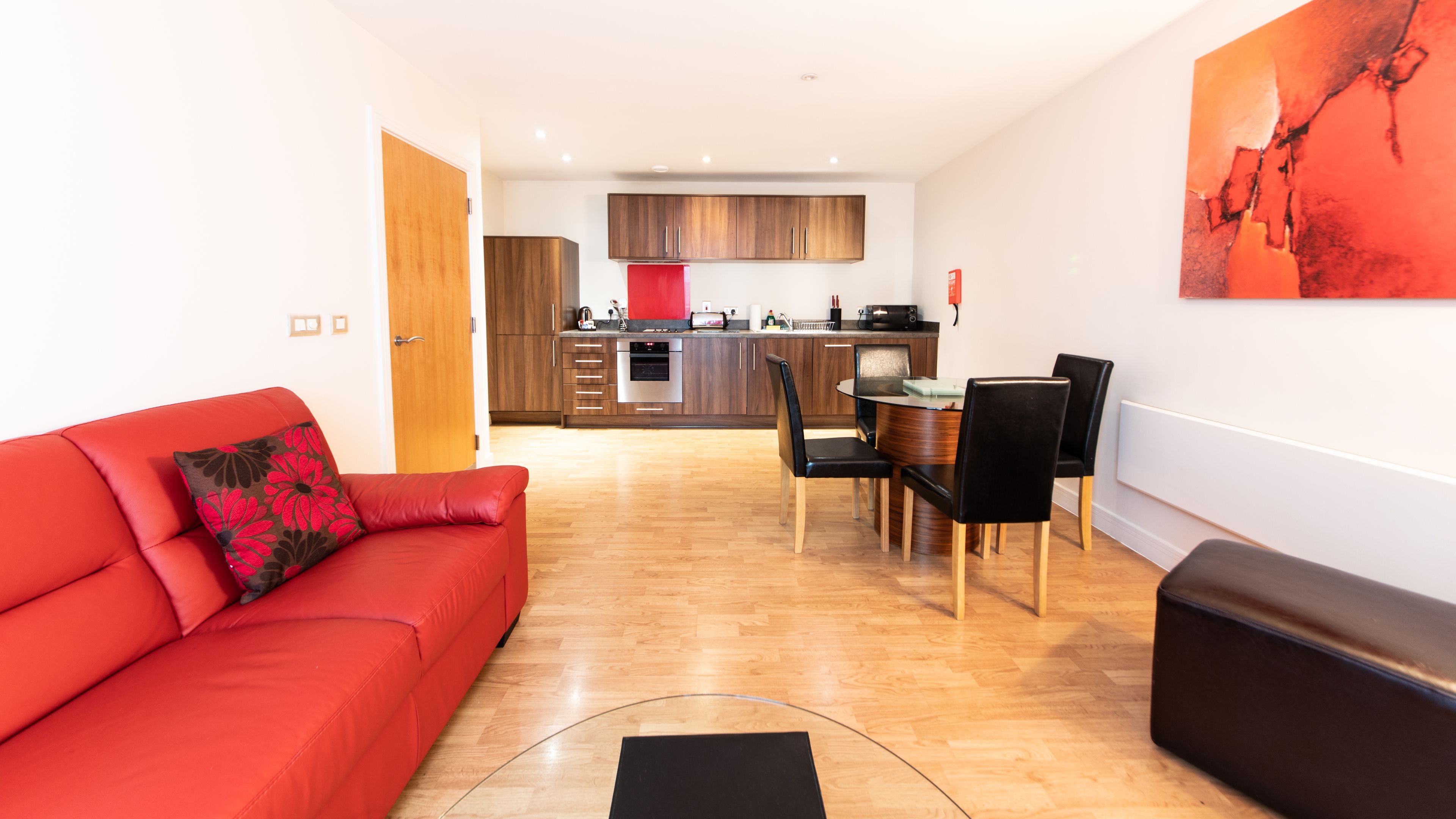 Una sala de estar moderna con un sofá rojo, un comedor con una mesa de vidrio y sillas, y una cocina con armarios de madera y un refrigerador rojo.