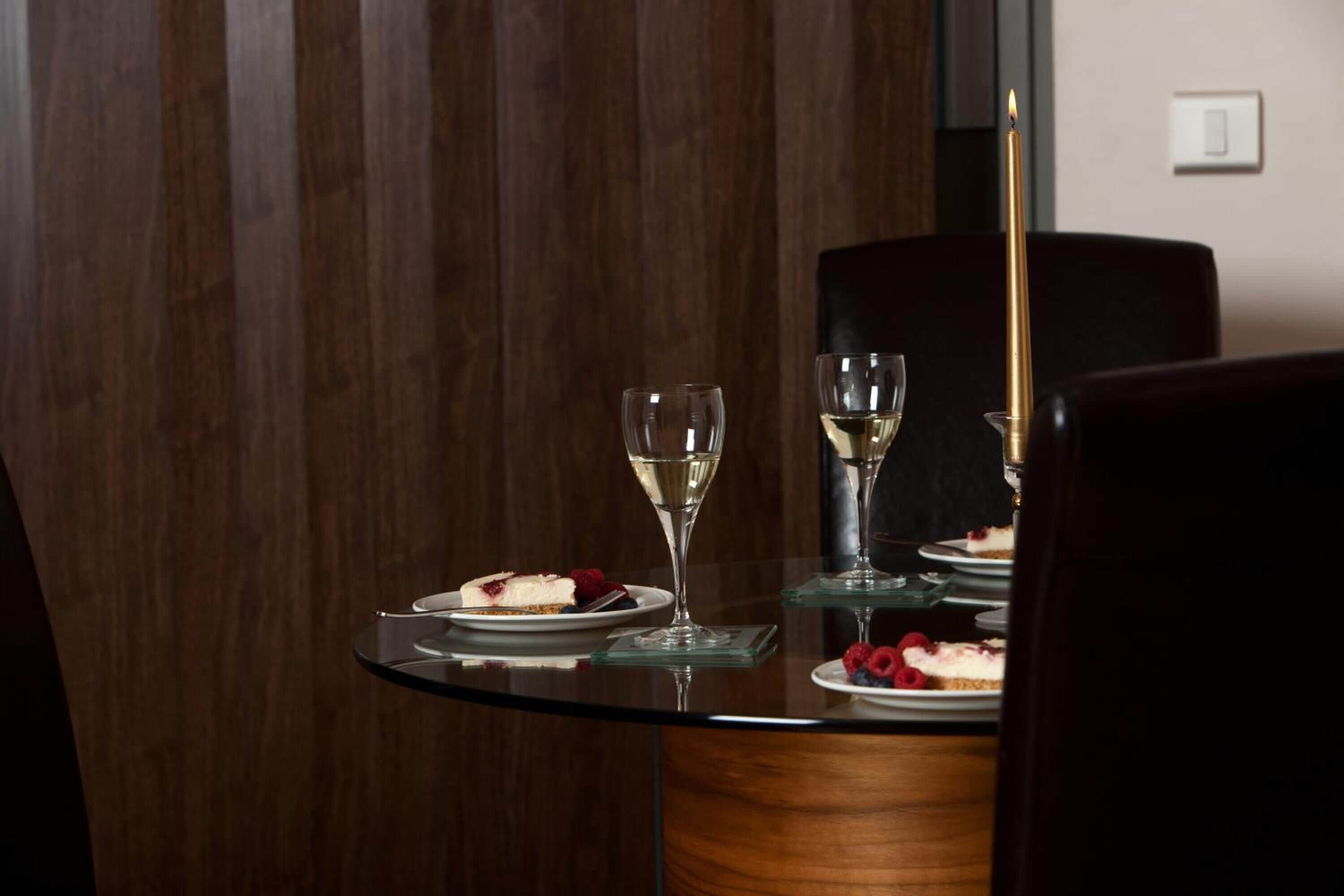 A dining table with two glasses of white wine, a candle, and plates with desserts.