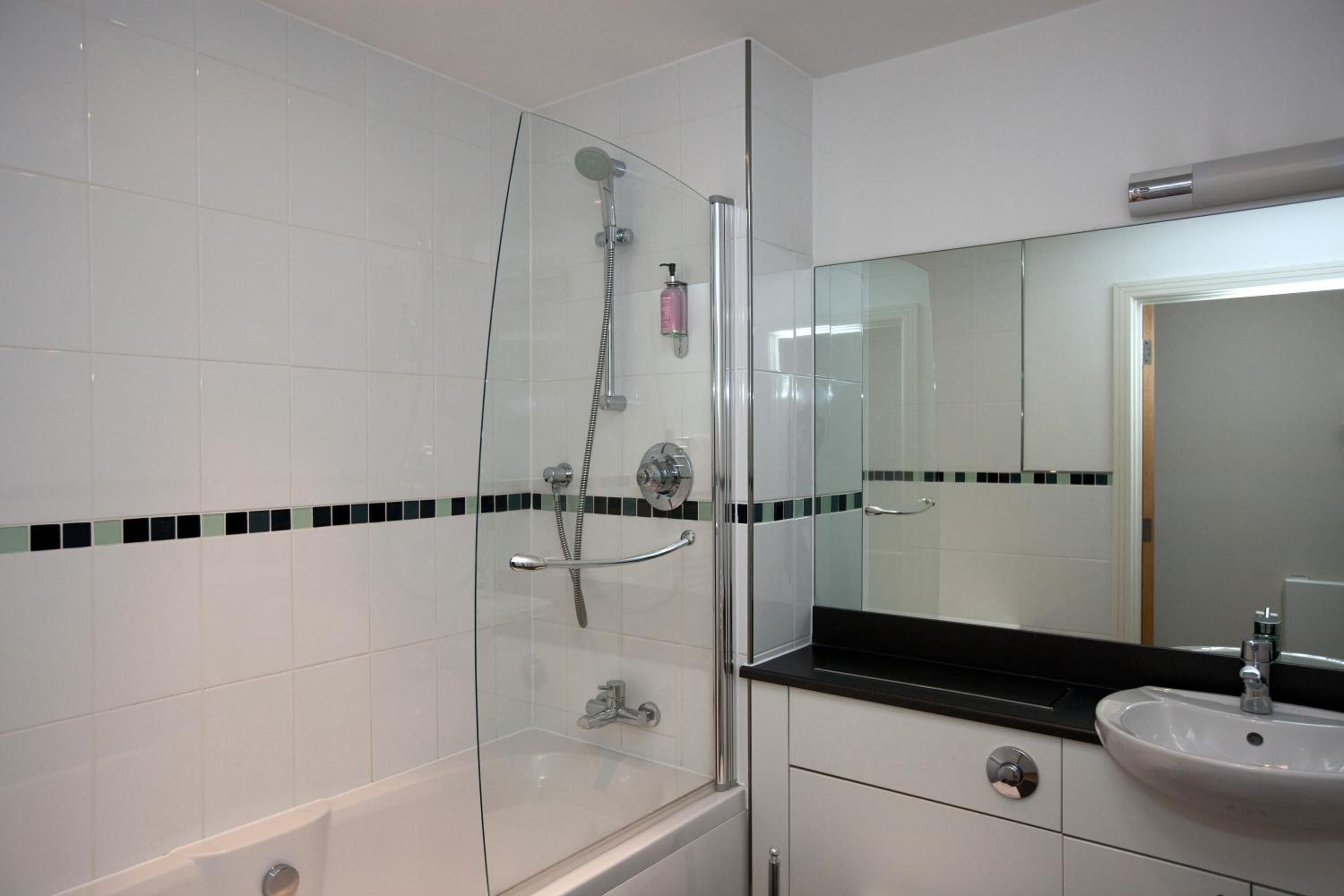Ein modernes Badezimmer mit einer gläsernen Duschkabine, einem weißen Waschbecken und einem Spiegel darüber.