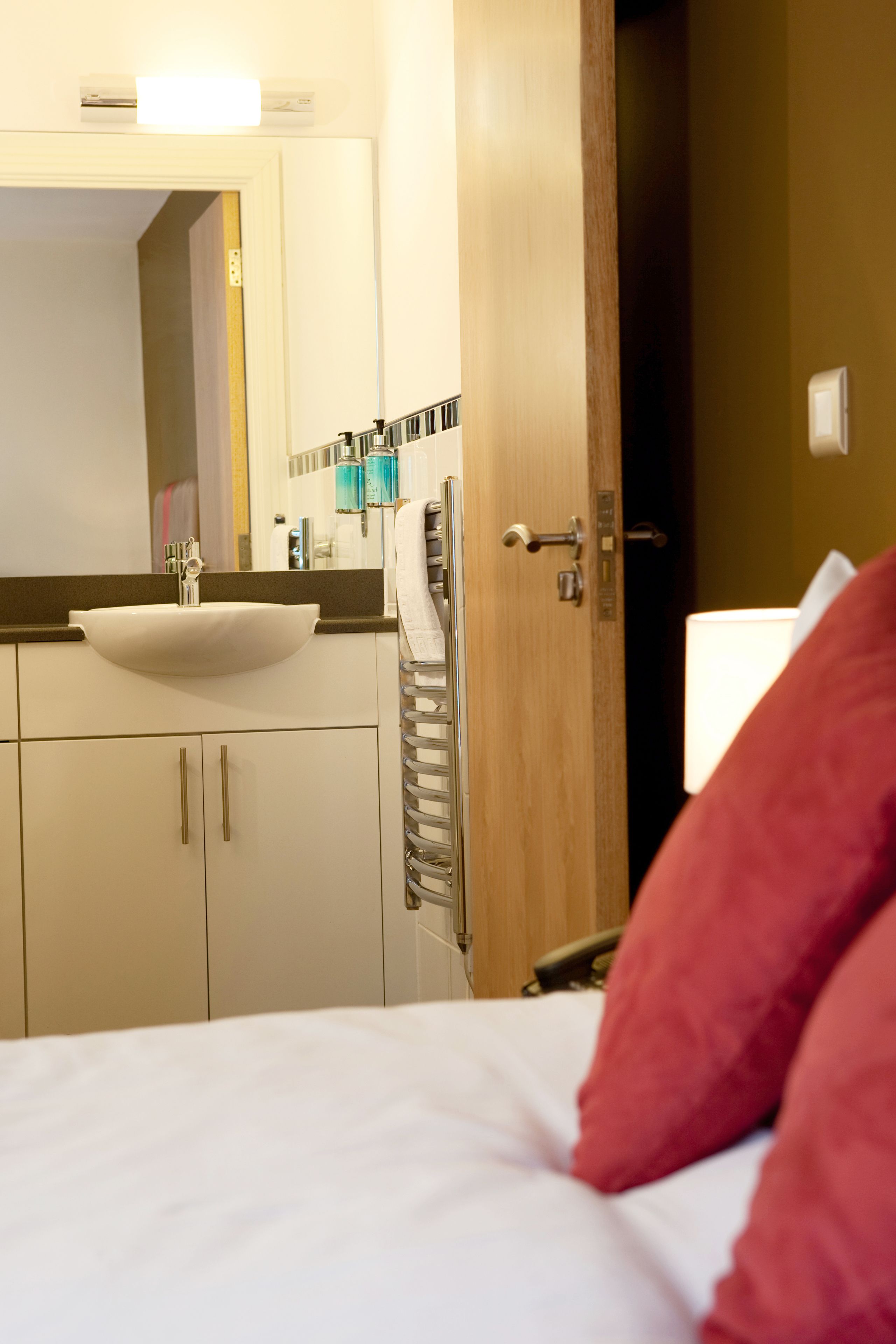 A hotel room with a bed, a white sink, a mirror, and a door leading to another room.