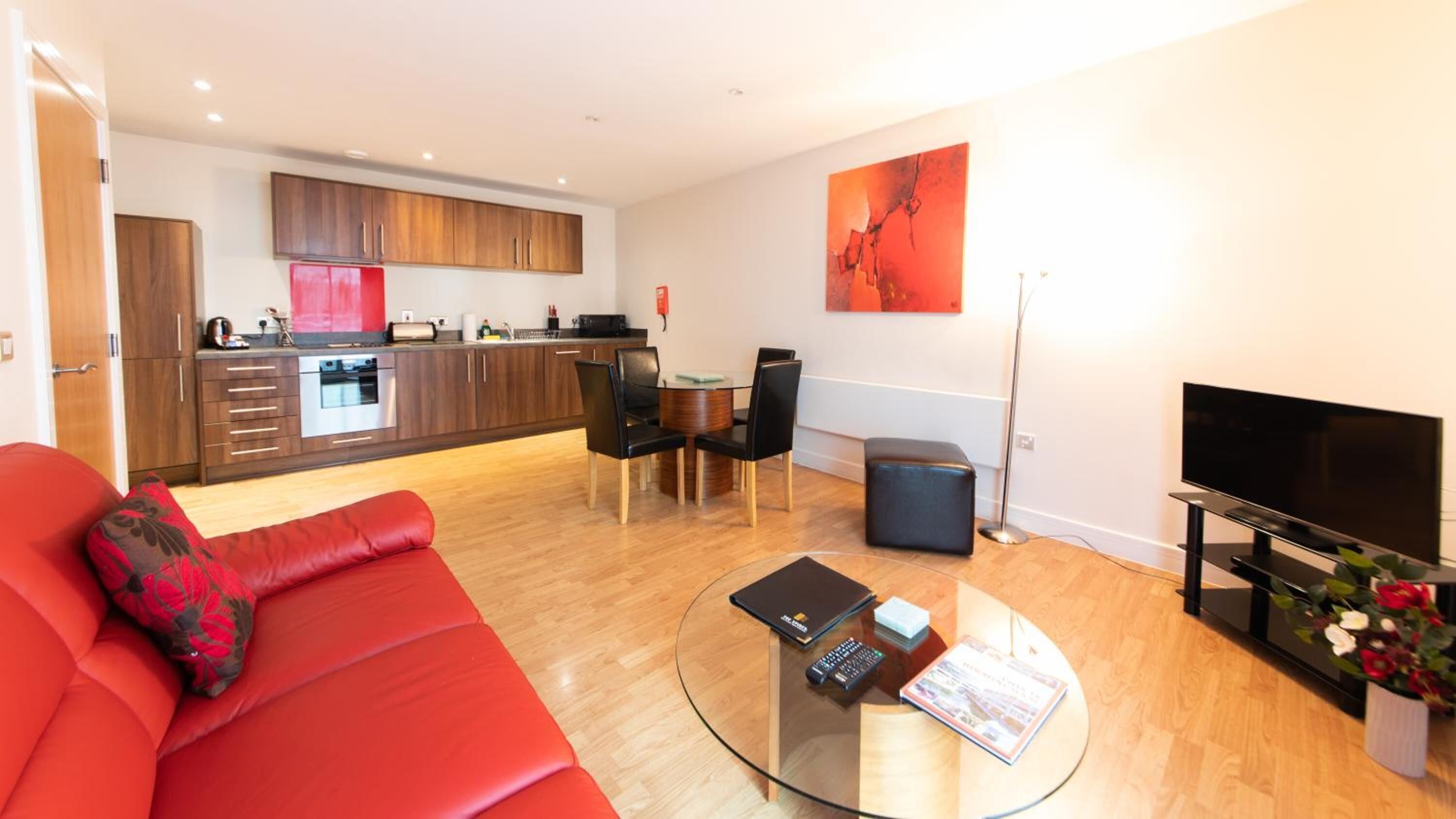 A modern living room with a red sofa, a glass coffee table, and a TV.