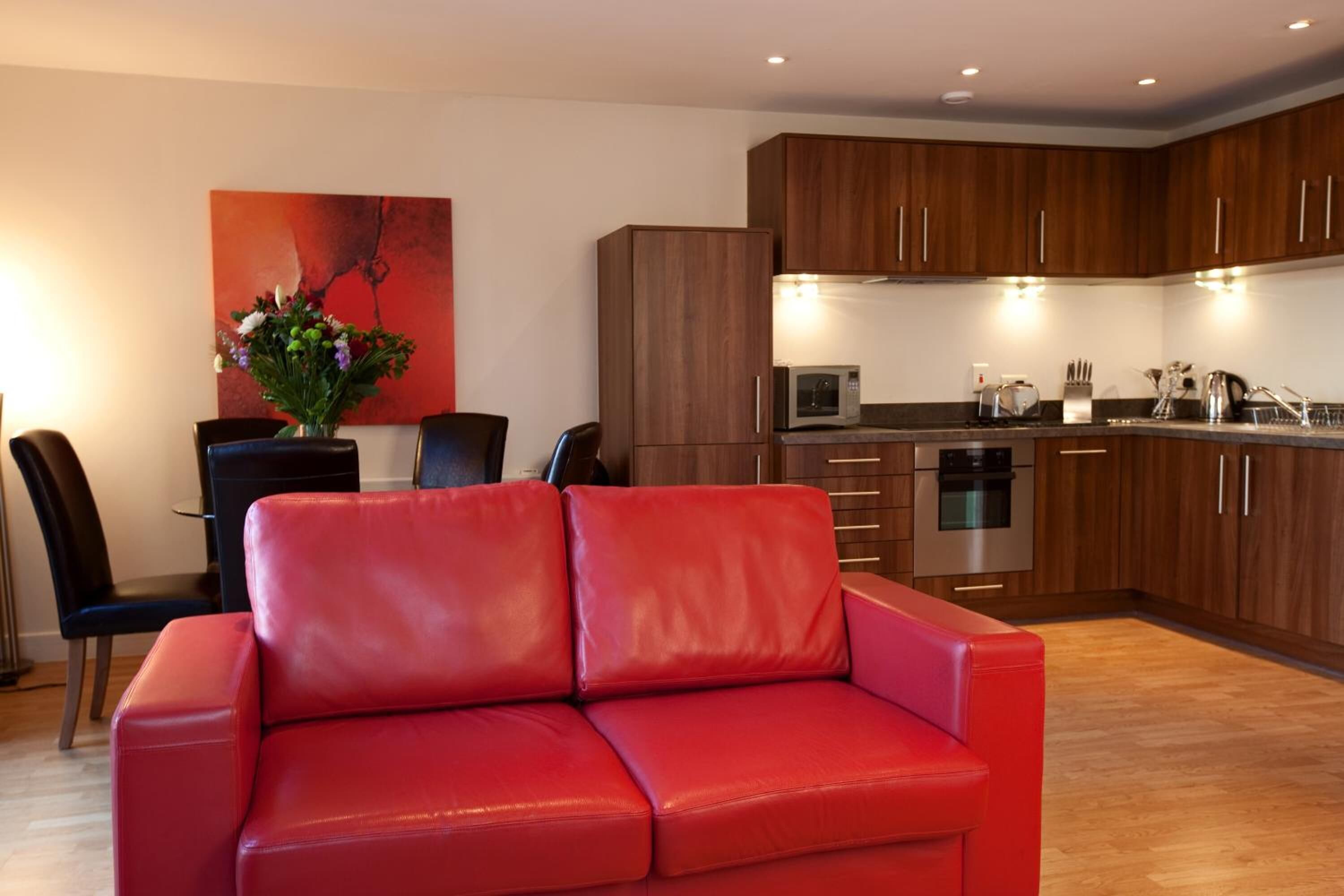 Una cocina moderna con armarios de madera, un sofá de cuero rojo y una zona de comedor con una silla negra y un jarrón de flores.