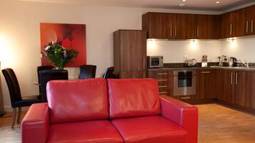 A modern kitchen with wooden cabinets, a red leather sofa, and a dining area with a black chair and a vase of flowers.