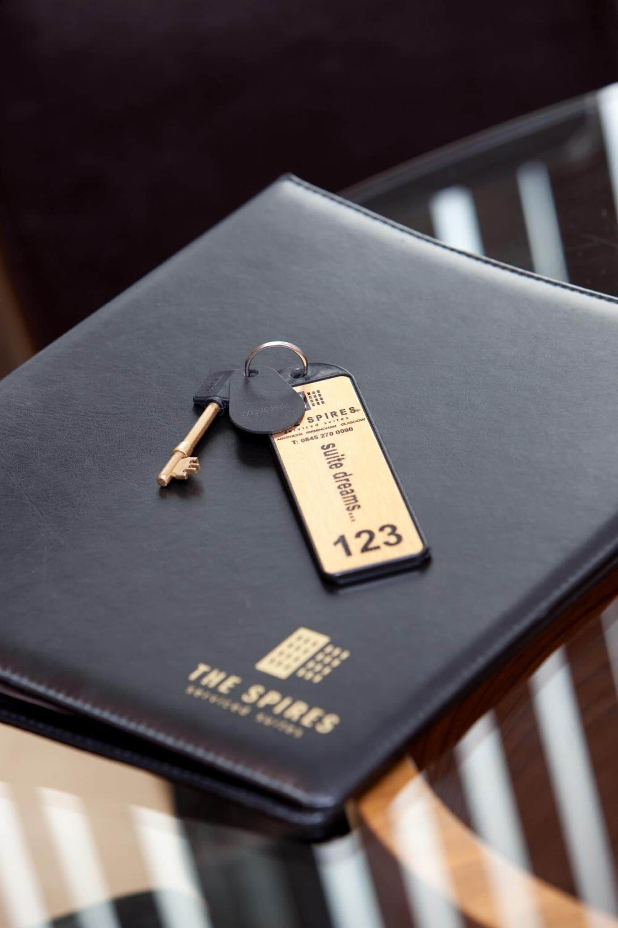 Un libro de tapa de cuero negro con un llavero dorado, que incluye una etiqueta con el número 123 y el texto 'The Spires'.