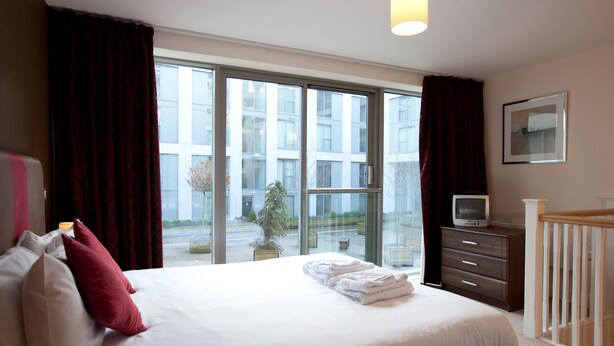 A hotel room with a large bed, a TV on a dresser, and a view of buildings outside. - The Spires Serviced Apartments Birmingham (Birmingham)