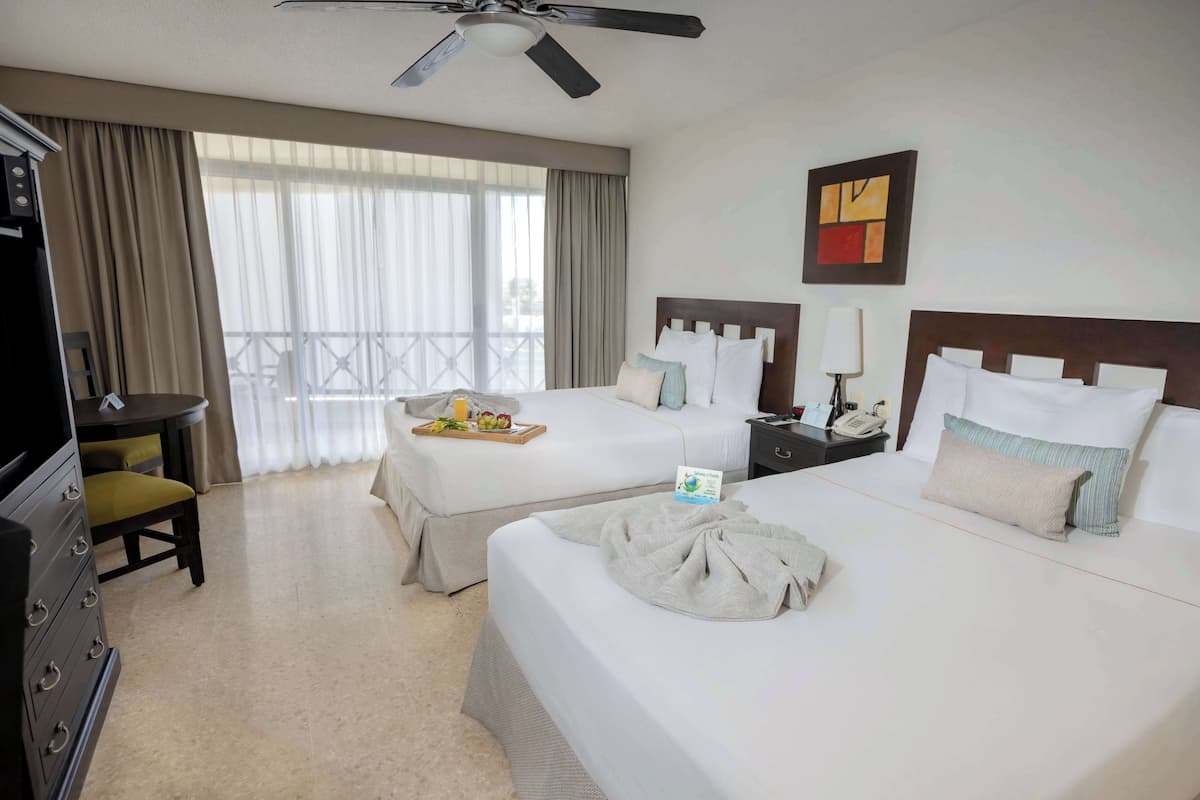 A hotel room with two beds, a desk, a chair, and a balcony with curtains.