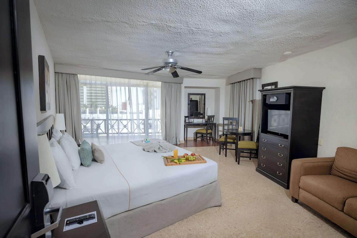 A hotel room with a bed, a TV, a desk, and a dining area.