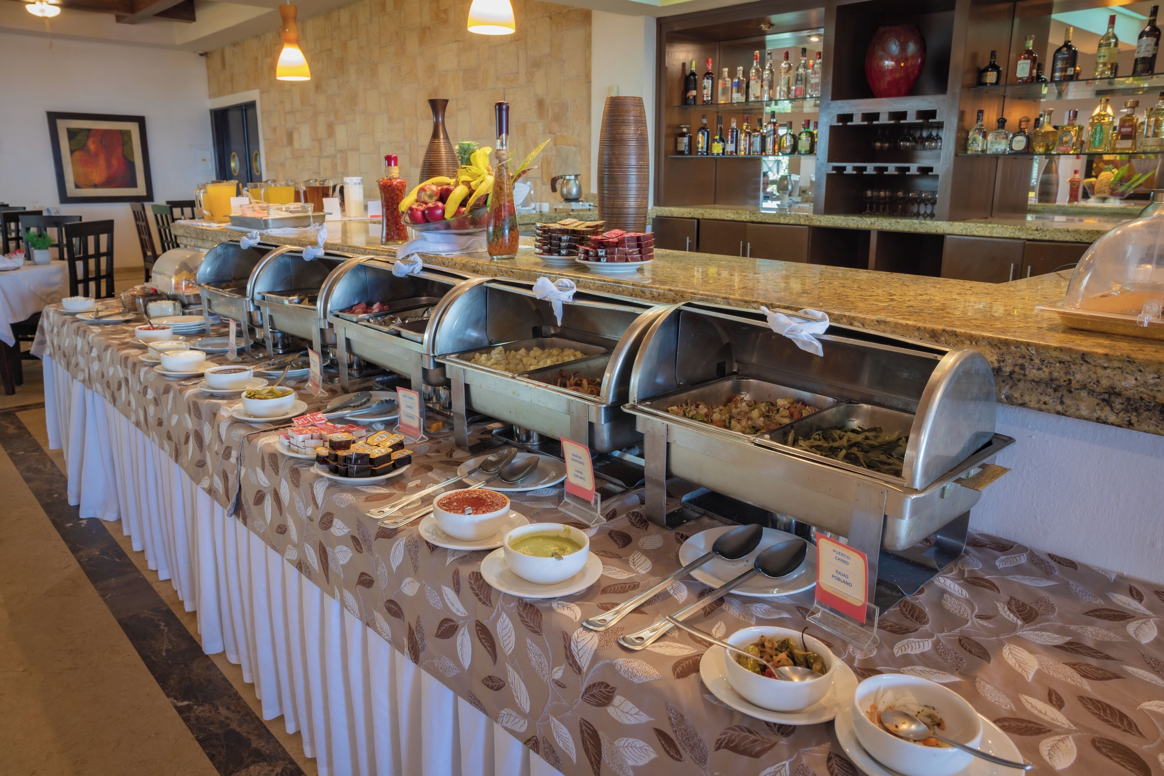 A buffet line with various food options, a bar area with liquor bottles, and a dining area with tables and chairs.