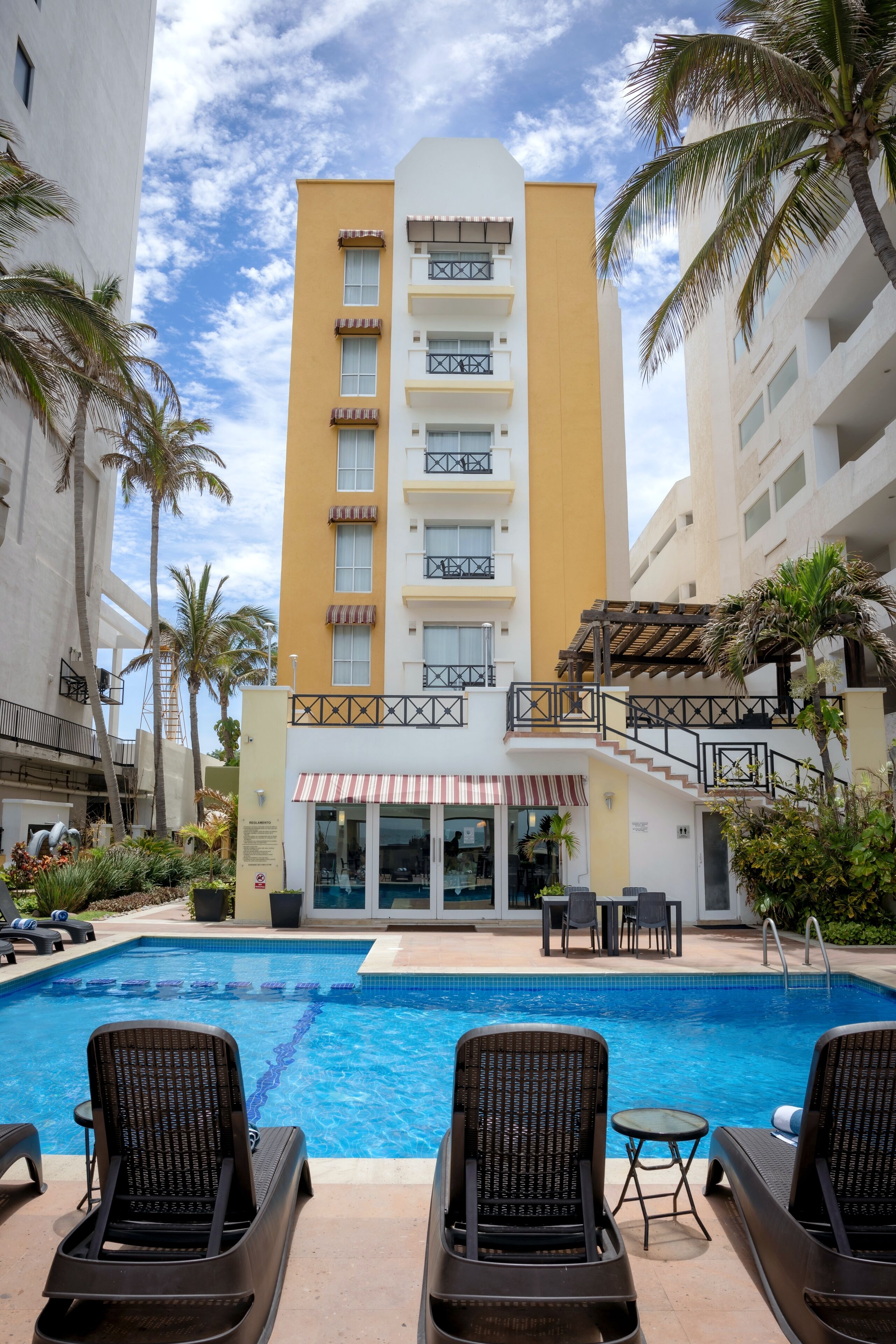 A hotel with a swimming pool, lounge chairs, and palm trees.
