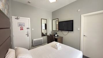 Habitación de hotel con cama, escritorio con silla, televisor y puerta con letrero de no fumar.