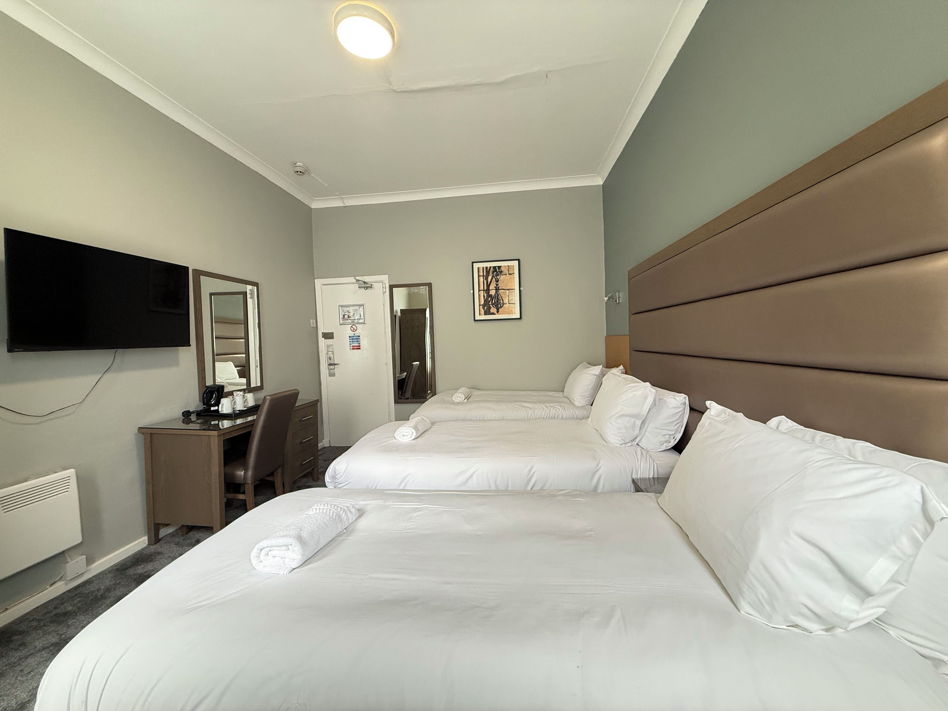 A hotel room with two beds, a desk, a chair, a television, and a door.
