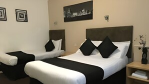 Une chambre d’hôtel avec deux lits simples et un lit plus grand, chacun étant équipé de draps noirs et blancs. On y trouve une table de chevet avec un vase de fleurs et une petite étagère avec une serviette.
