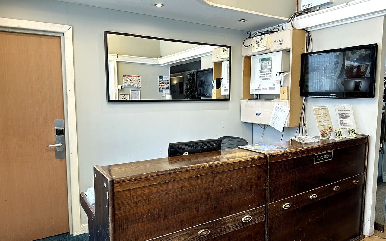 Una mesa de recepción con un espejo, un televisor y un mueble de madera con la etiqueta 'Reception'.