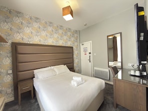 Habitación de hotel con una cama grande, una mesita de noche, un escritorio con espejo y un televisor montado en la pared.