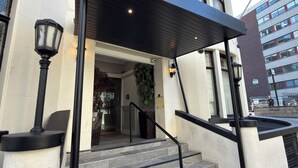 Une entrée d’immeuble avec un escalier couvert, un pot de fleurs et une caméra de surveillance.