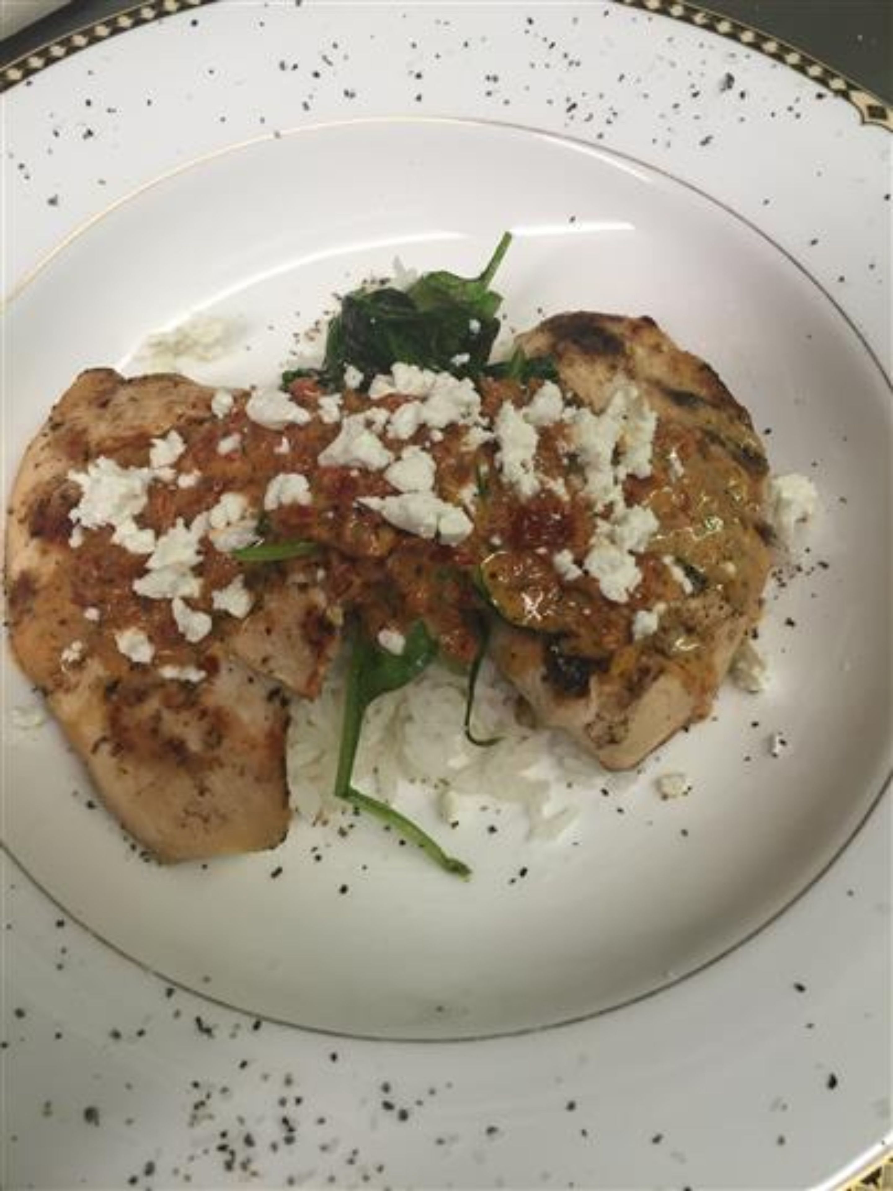 A plate with grilled chicken, feta cheese, and greens.