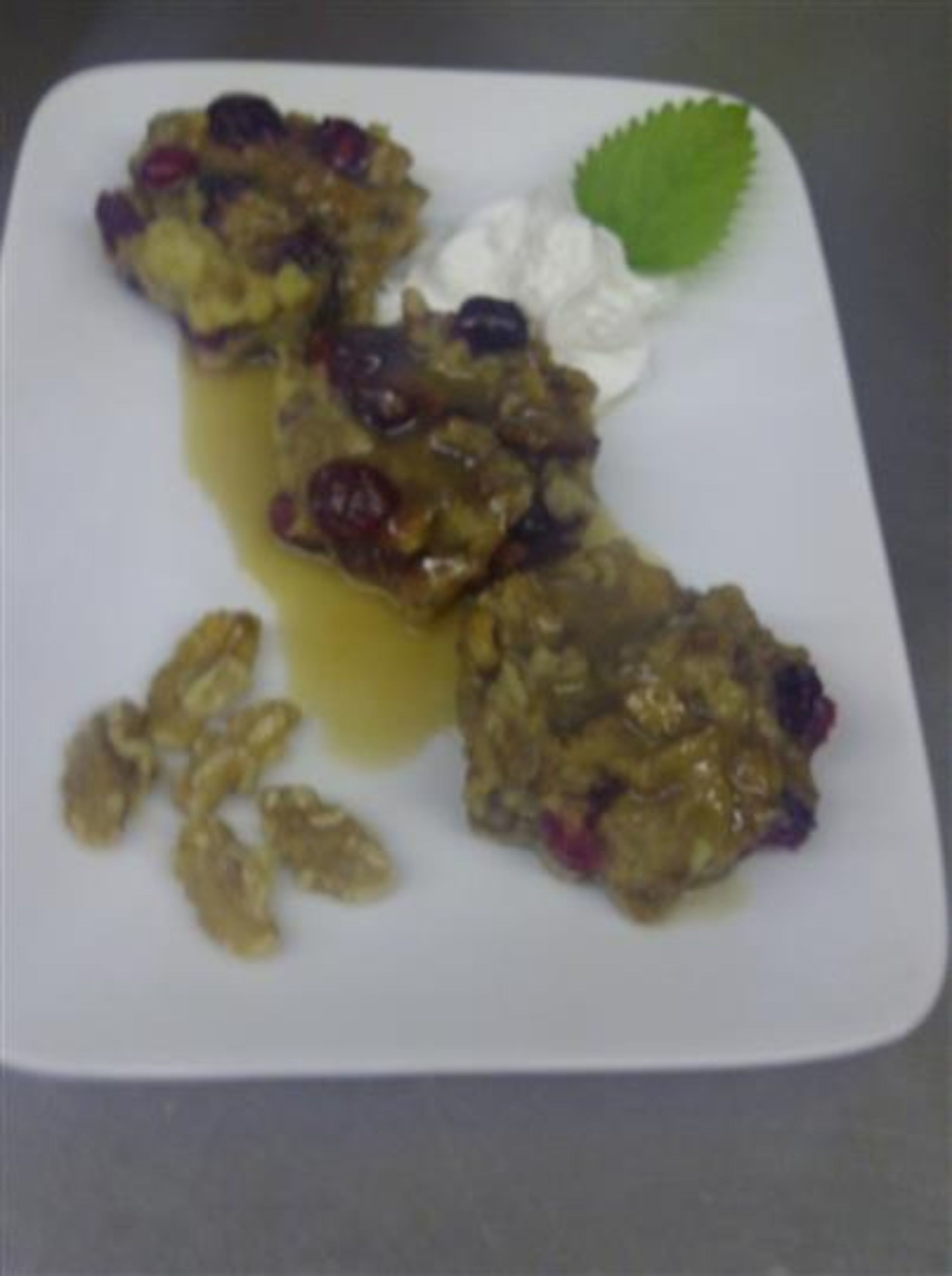 Une assiette contenant un dessert composé d’une compote de fruits, d’une cuillerée de crème et d’une feuille verte en guise de décoration.
