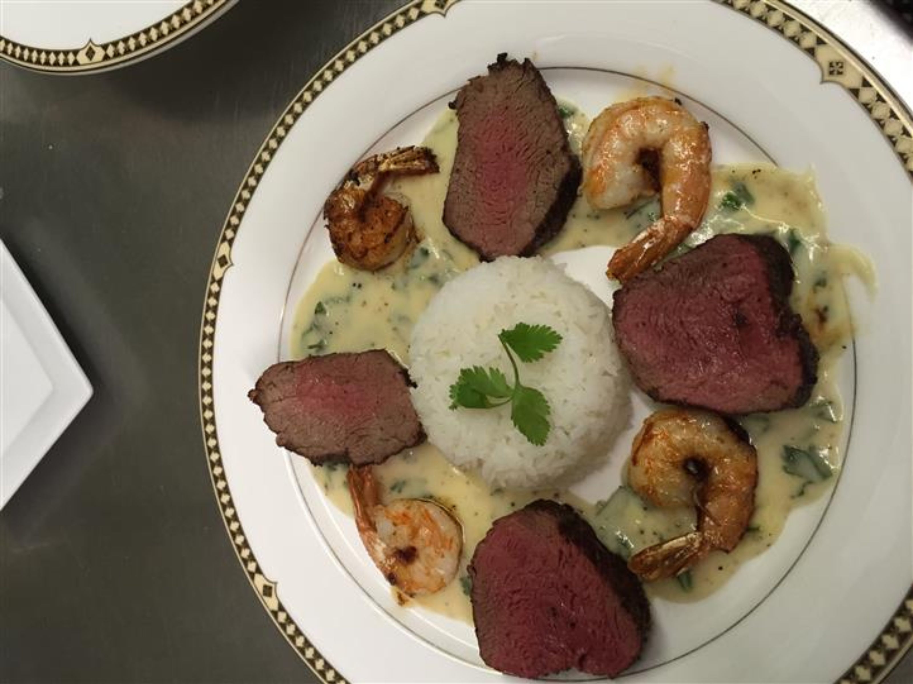 Un plato de comida con bisteck, camarones y arroz.