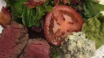 A plate with a salad, a slice of tomato, a piece of meat, a boiled egg, and a dollop of blue cheese.