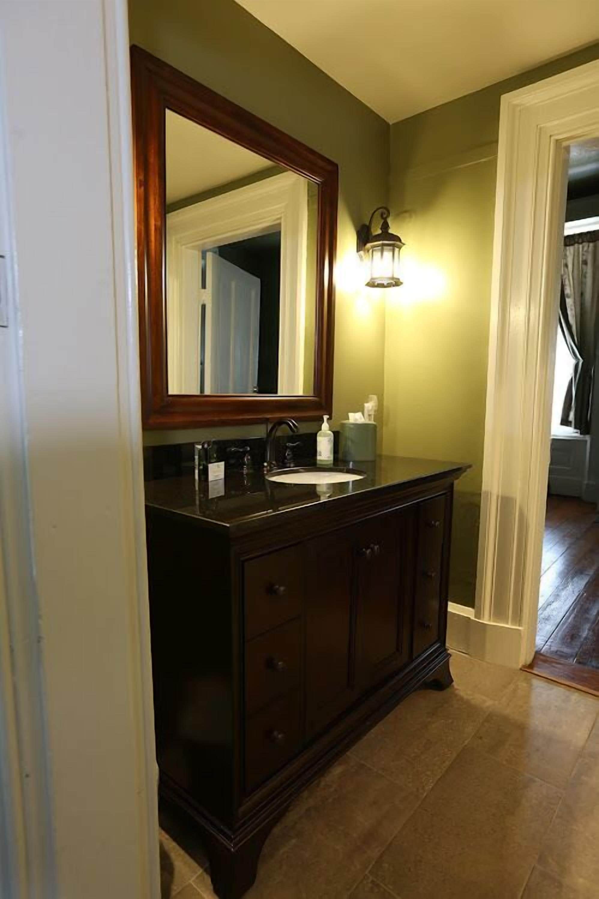 A bathroom with a dark wooden vanity, a large mirror, and a wall-mounted light fixture.