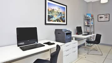 A modern office with a desktop computer, printer, and a chair. There is a framed picture of a cityscape on the wall.