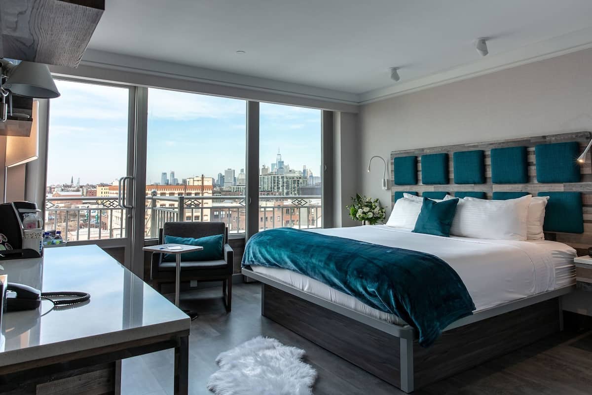 Una habitación de hotel moderna con una cama grande, un escritorio, una silla y vistas a la ciudad.