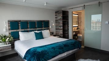 A modern bedroom with a large bed, a wooden headboard, and a view of the city through a glass door.