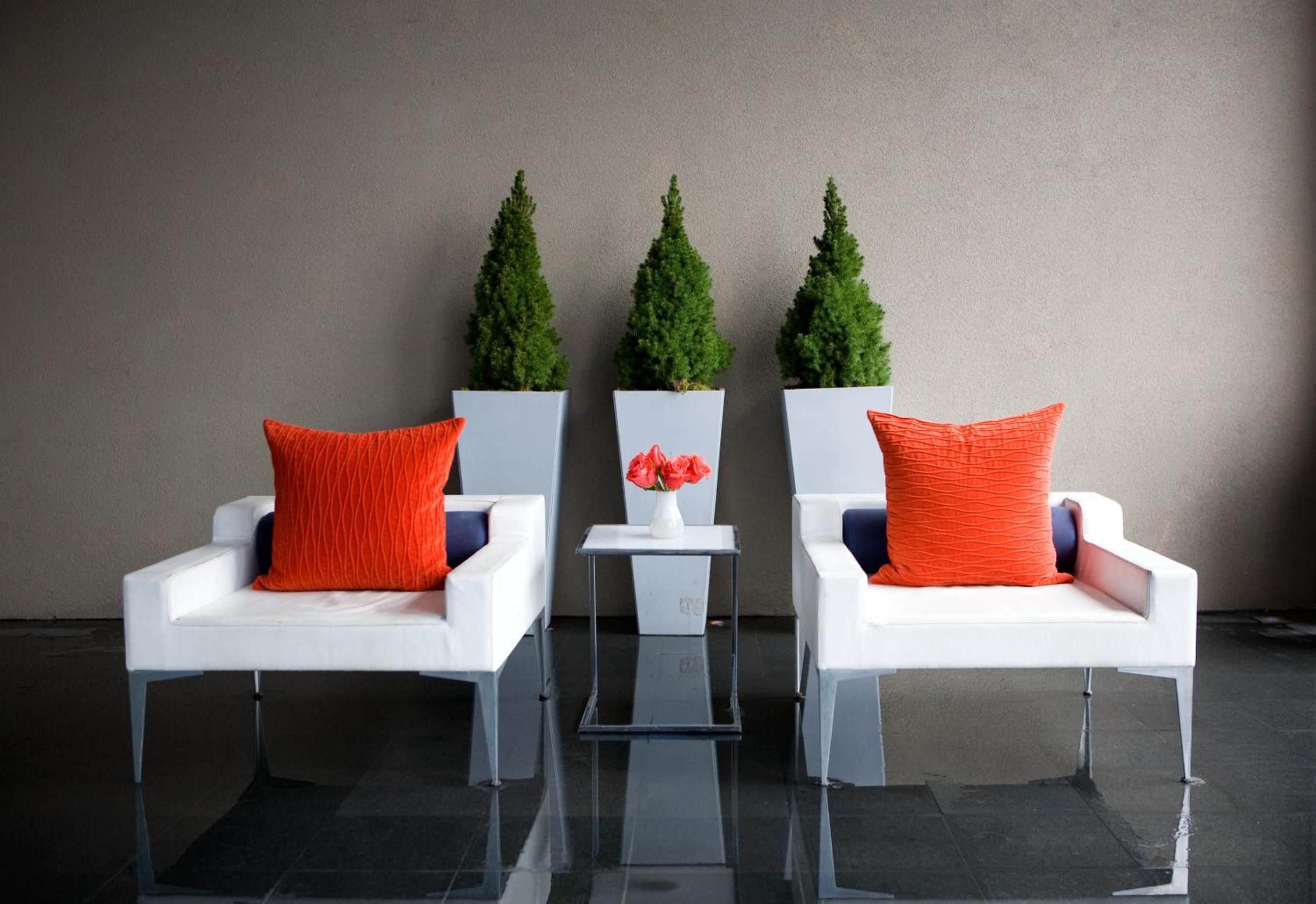 Three white chairs with orange cushions and a small table with a vase of flowers between them.