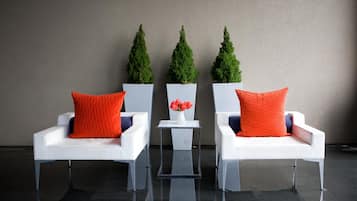Three white chairs with orange cushions and a small table with a vase of flowers between them.