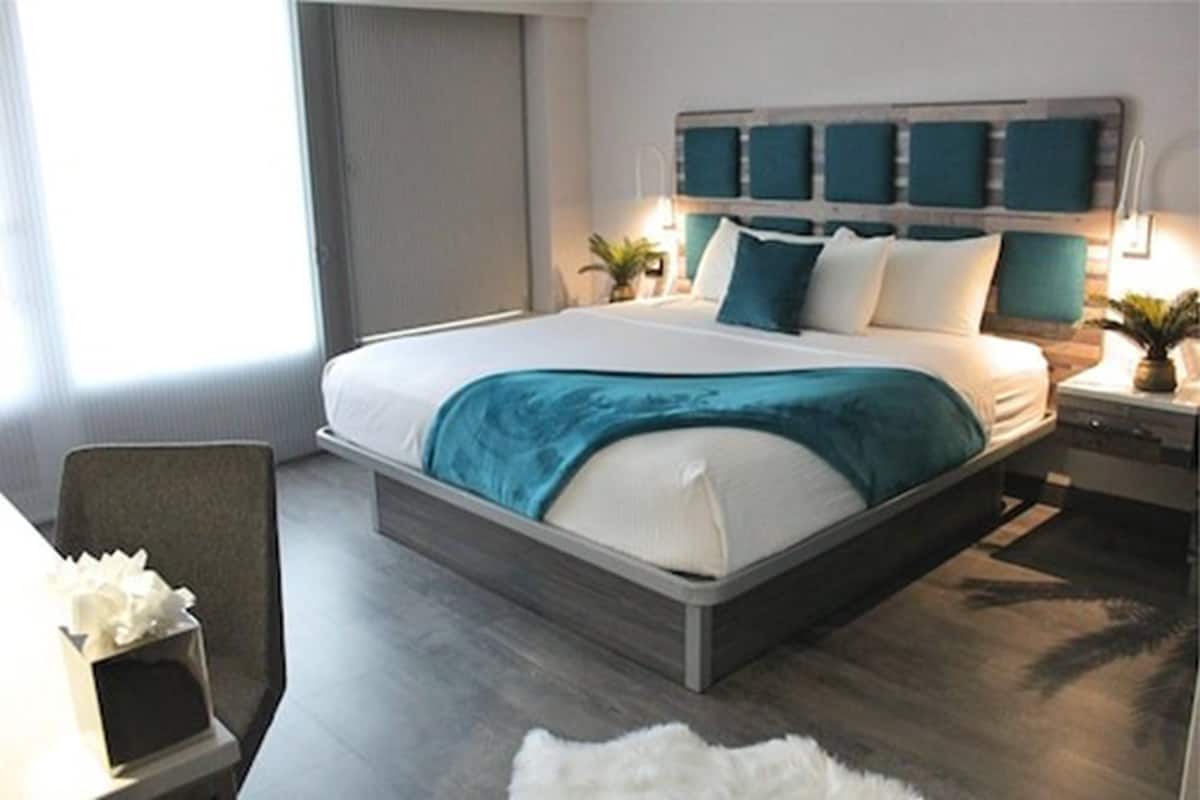 Una habitación de hotel moderna con una cama grande, un cabecero de madera y una mesita de noche con una lámpara.