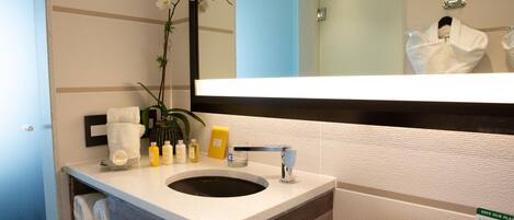 A modern bathroom with a wooden vanity, a sink, and a toilet. There is a mirror above the sink, and a plant is placed on the vanity.