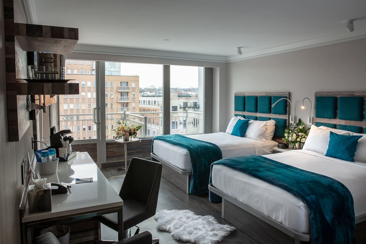 Habitación de hotel con dos camas, un escritorio, una silla y vistas a la ciudad.