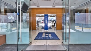 A hotel entrance with a glass door, a blue carpet with the hotel name, and a view into the lobby. - Hotel Le Bleu (Brooklyn)