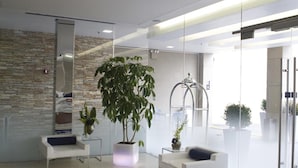 A modern reception area with a glass wall, a large potted plant, and a blue carpet with a logo. - Hotel Le Bleu (Brooklyn)