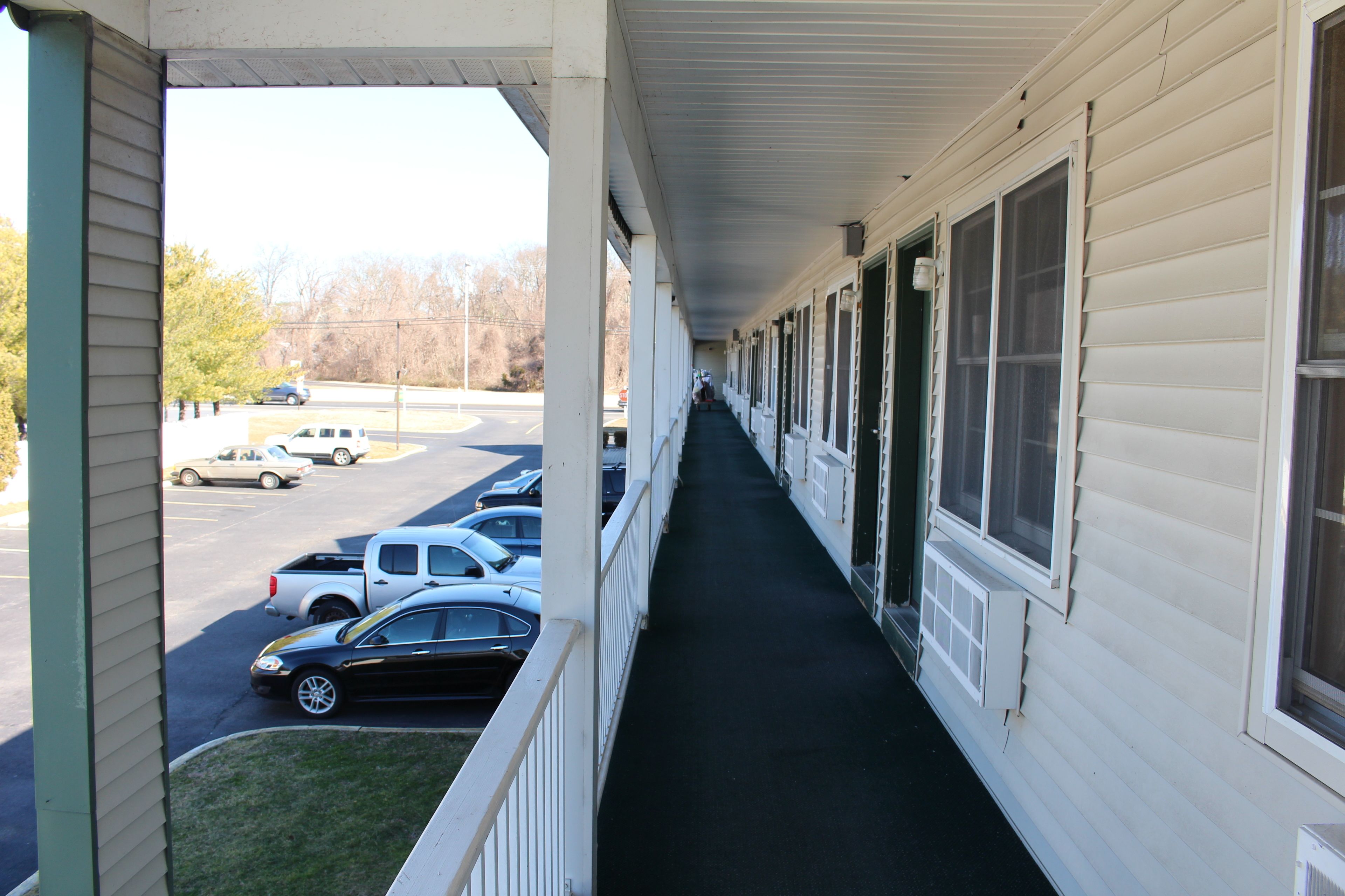 A motel corridor with a covered walkway, parking lot, and a view of the street.