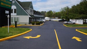 A parking lot with directional arrows, a Highlander Motor Inn building, and a few parked cars. - Highlander Motor Inn Atlantic City (Absecon)