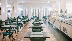 Una amplia cafetería con filas de mesas y sillas, un mostrador de buffet a la derecha y grandes ventanales que dejan entrar luz natural.