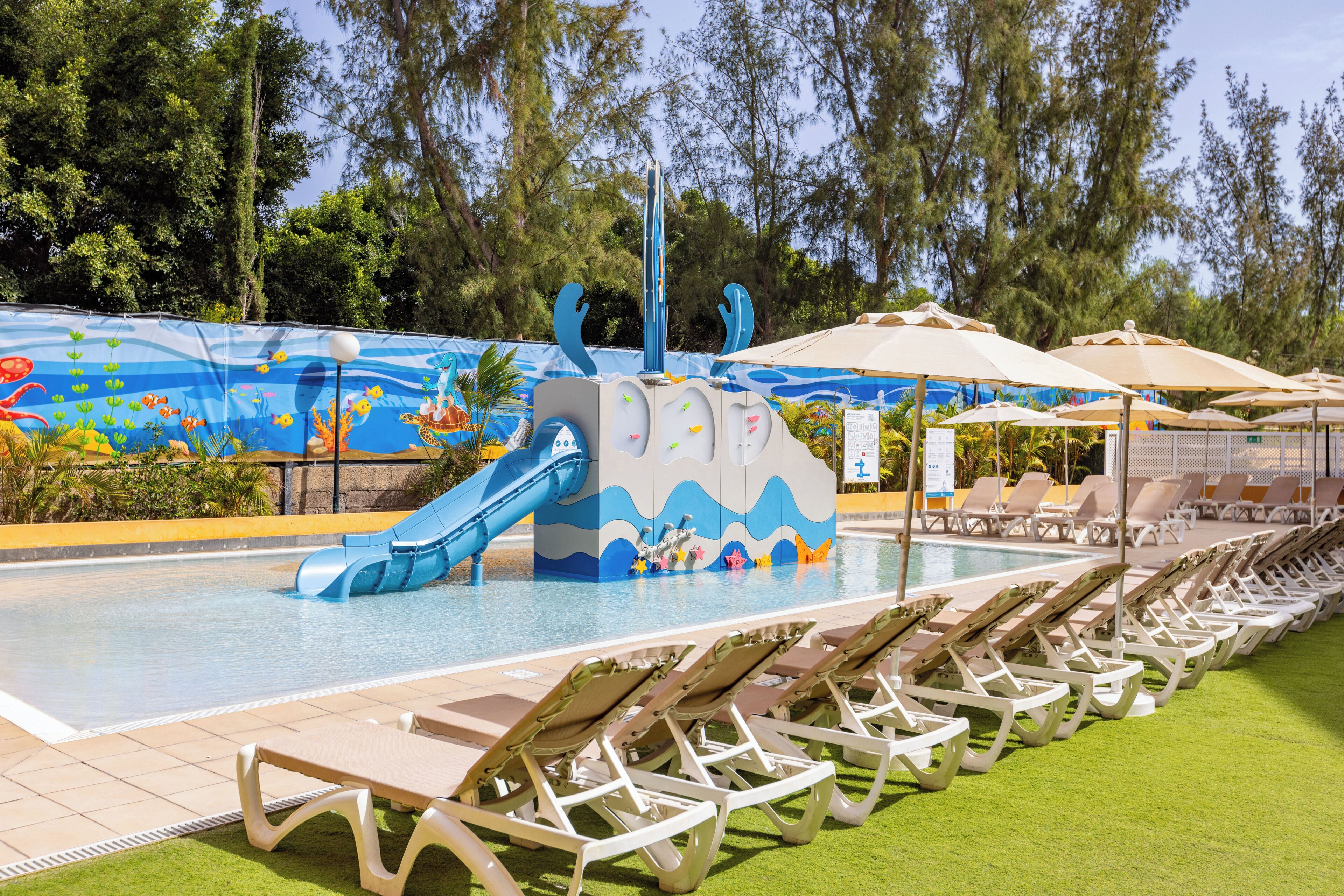 A pool area with a slide, lounge chairs, and a mural of underwater scenery.