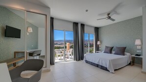 Una habitación de hotel moderna con una cama grande, un escritorio, una silla y un balcón con vistas a la ciudad y a las montañas.
