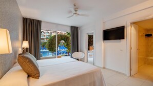Habitación de hotel con cama, ventilador de techo, televisión y vista a una piscina y edificios.