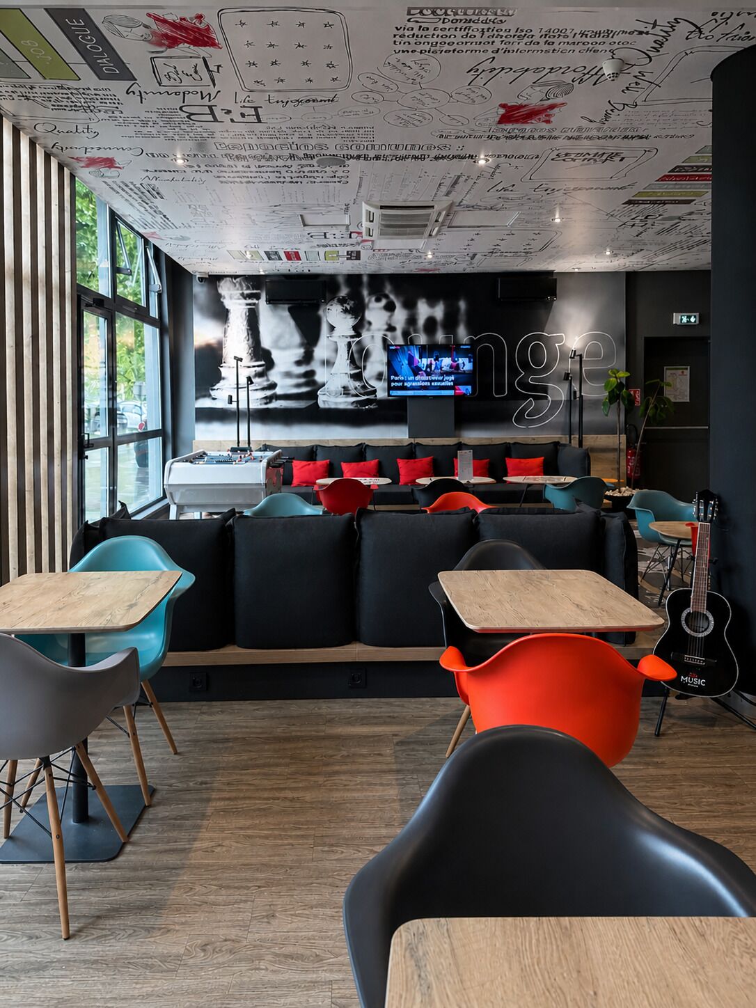 A modern cafe with a chessboard mural, a large TV screen, and a mix of black and colorful seating.
