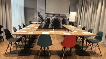 A conference room with a long table, chairs, a projector screen, and a mural of a building.
