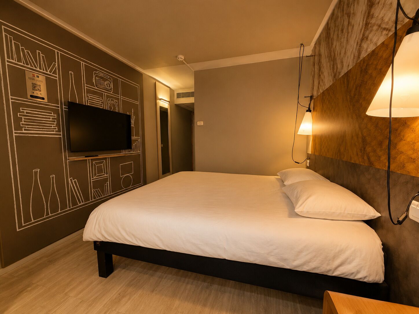 Un dormitorio con cama, televisor de pantalla plana en la pared y lámpara adosada a la pared.