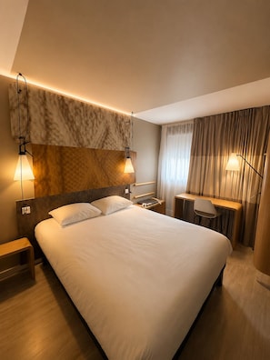 A modern hotel room with a large bed, bedside tables, a desk, and a chair.