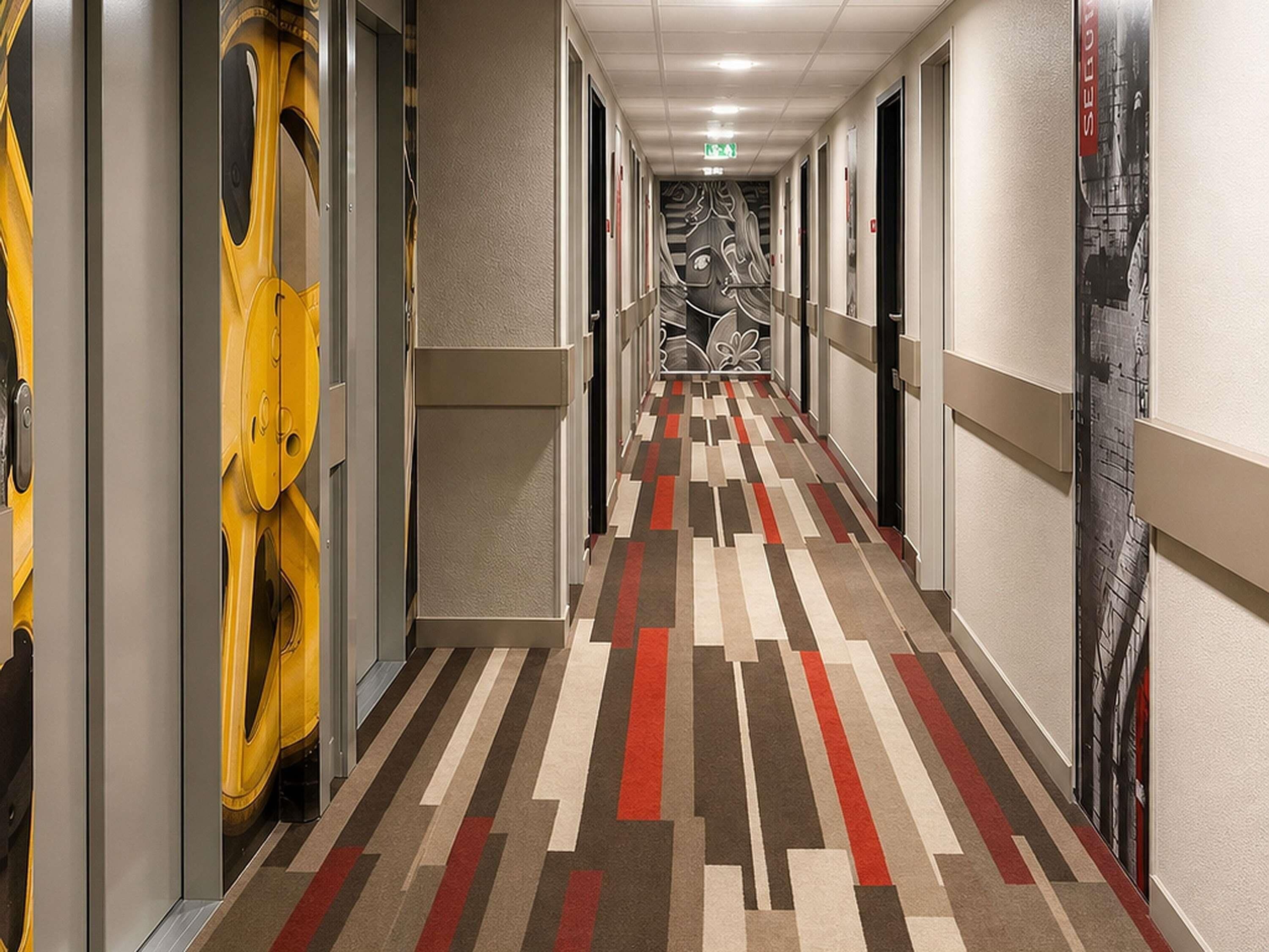 A hotel hallway with patterned carpet, doors, and a wall with a graphic design.